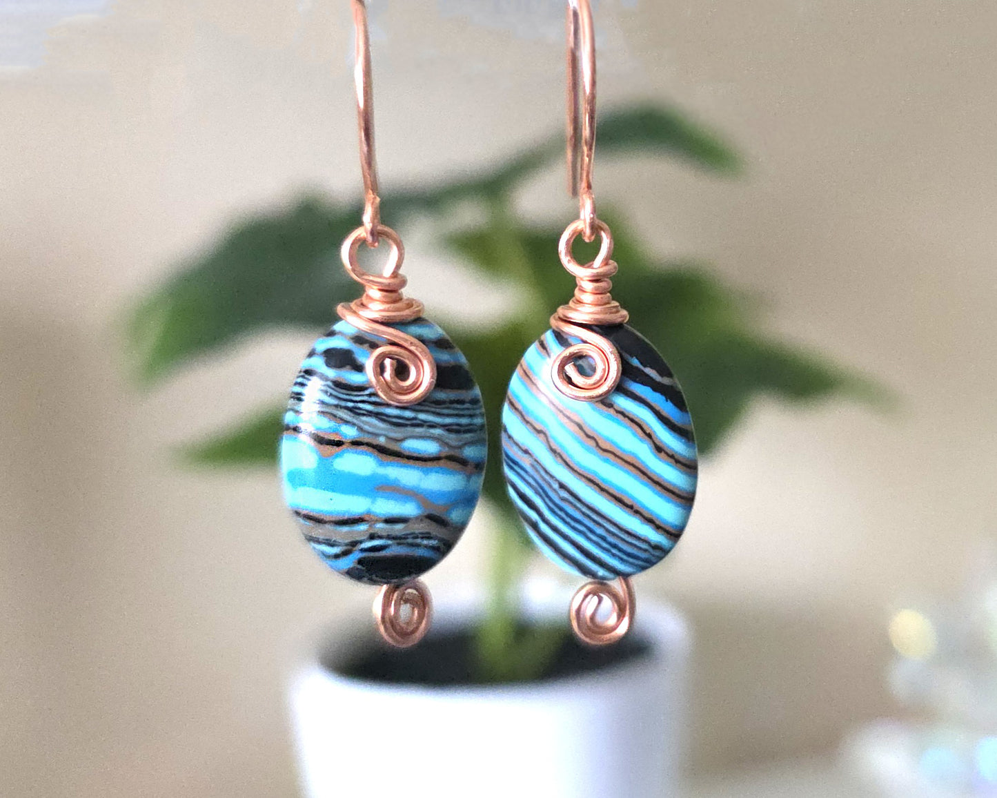 Celtic style marbled multi color copper earrings with coils and french earring hooks with white with plant background 