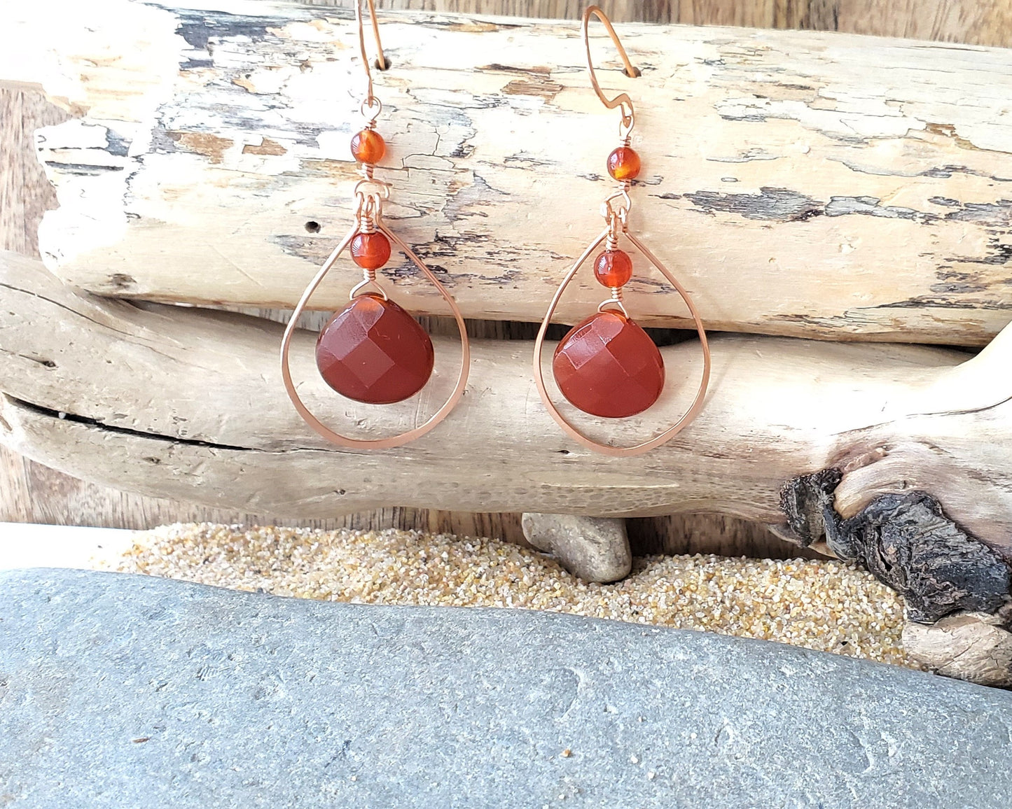 Long handmade copper earrings with large drop shaped orange/brown color carnelian stones and drop shaped copper hoops on french earring hooks on wood