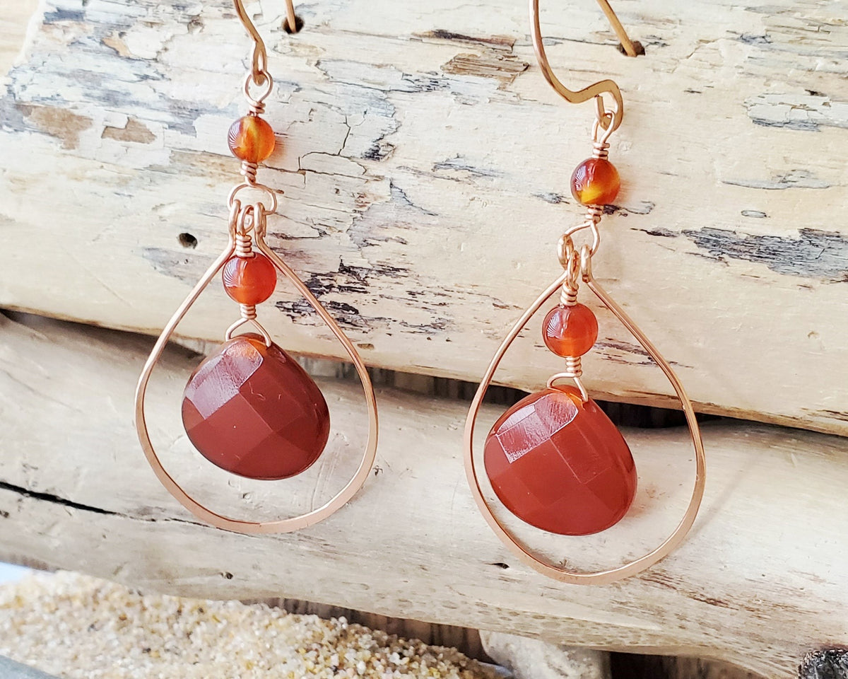 Long handmade copper earrings with large drop shaped orange/brown color carnelian stones and drop shaped copper hoops on french earring hooks on wood