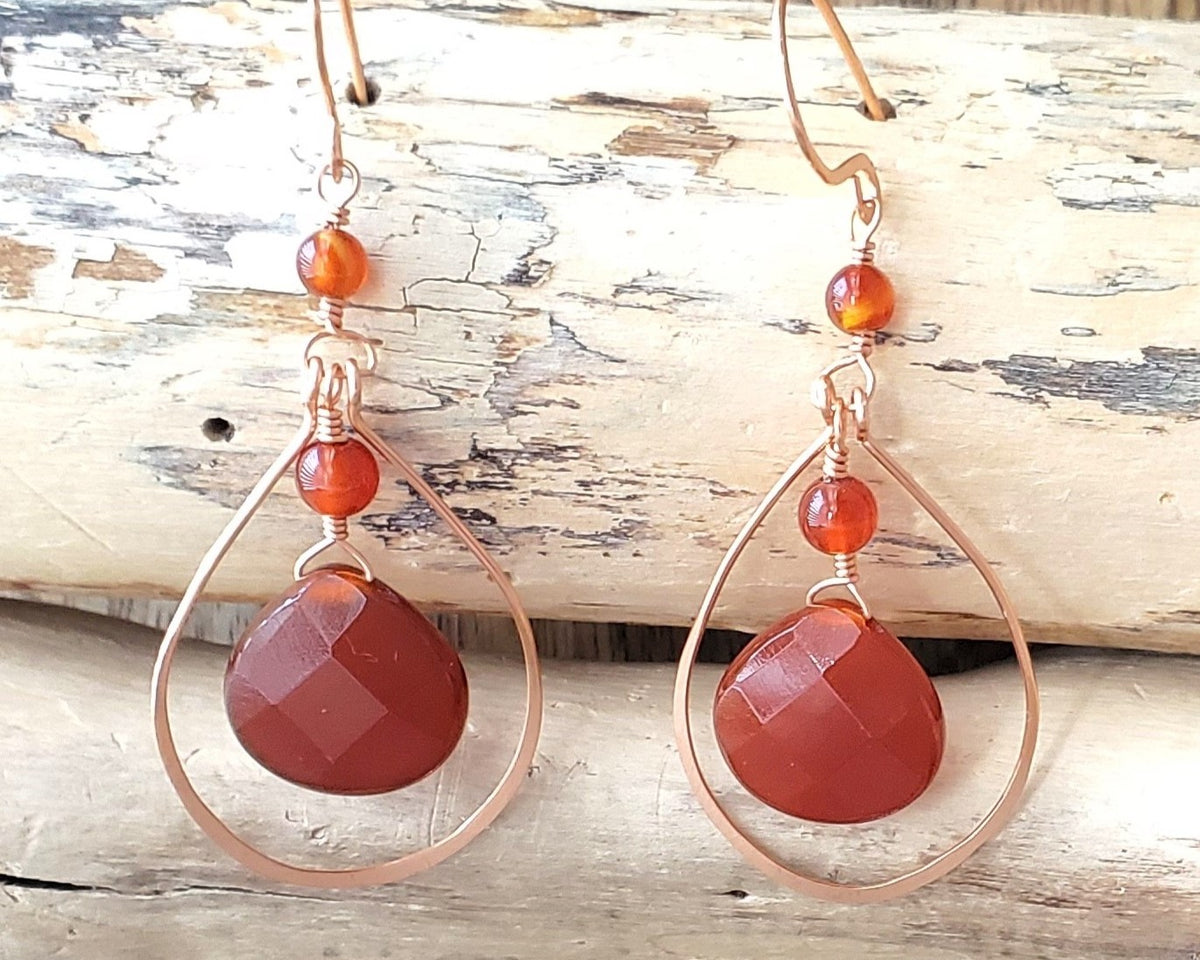 Long handmade copper earrings with large drop shaped orange/brown color carnelian stones and drop shaped copper hoops on french earring hooks on wood