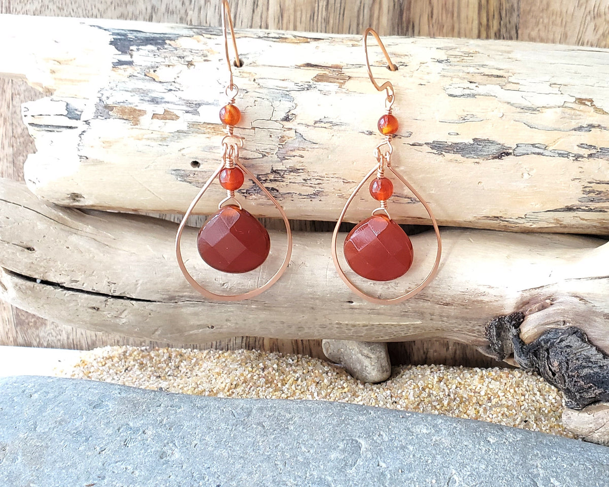 Long handmade copper earrings with large drop shaped orange/brown color carnelian stones and drop shaped copper hoops on french earring hooks on wood
