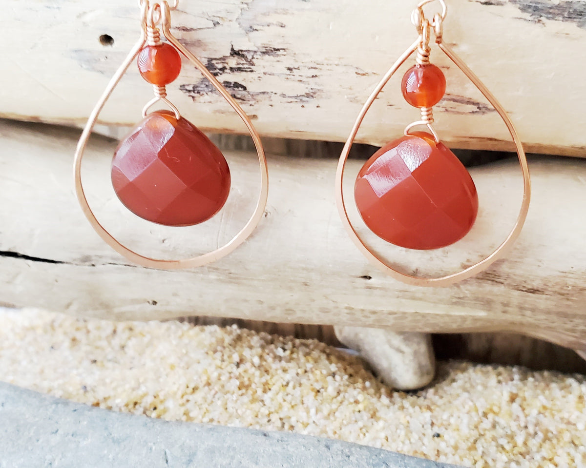 Long handmade copper earrings with large drop shaped orange/brown color carnelian stones and drop shaped copper hoops on french earring hooks on wood