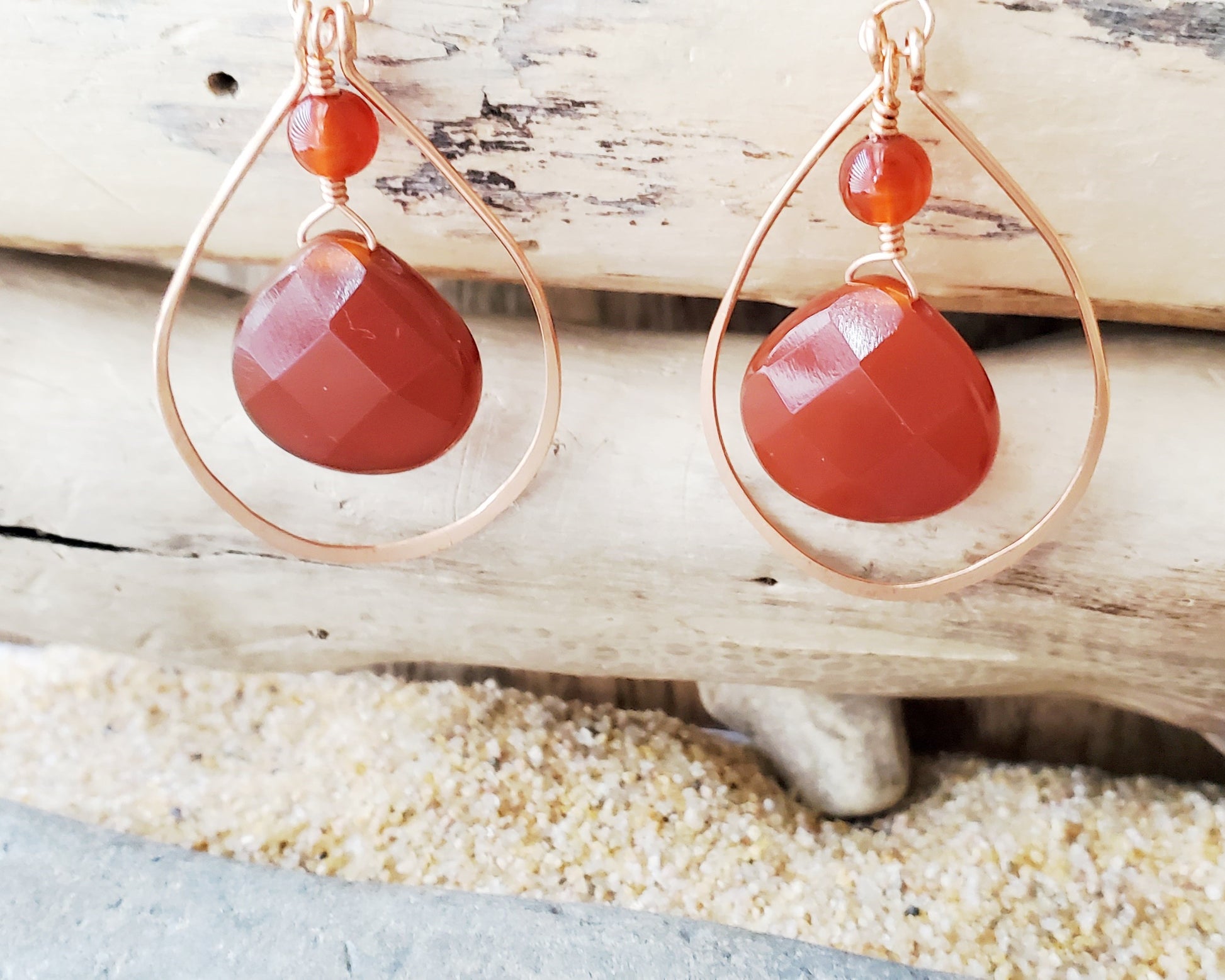 Long handmade copper earrings with large drop shaped orange/brown color carnelian stones and drop shaped copper hoops on french earring hooks on wood