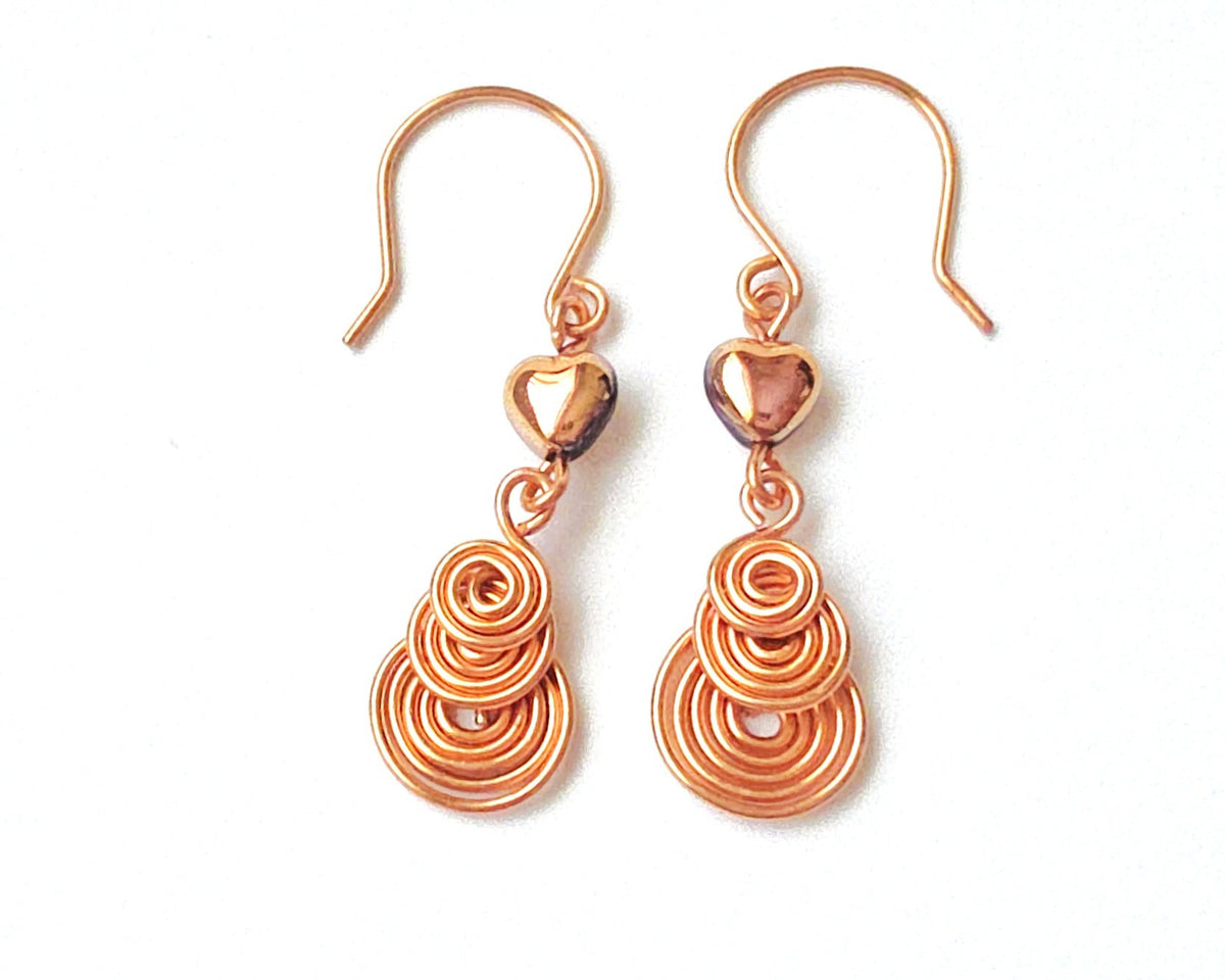 A pair of handmade copper earrings with three coil pendants and gold hearts with french earrings hooks on white background  