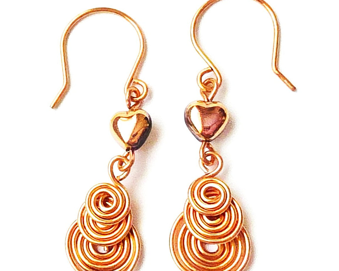 A pair of handmade copper dangle earrings with three coil pendants and gold hearts with french earrings hooks on white background  