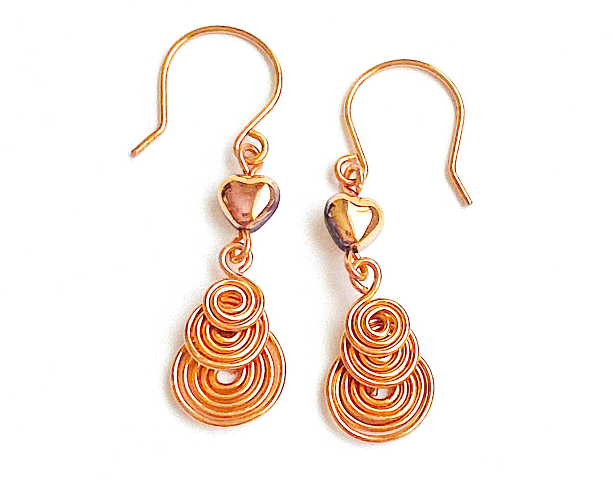 A pair of handmade copper dangle earrings with three coil pendants and gold hearts with french earrings hooks on white background   