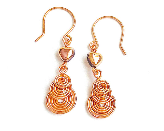 A pair of handmade copper dangle earrings with three coil pendants and gold hearts with french earrings hooks on white background   
