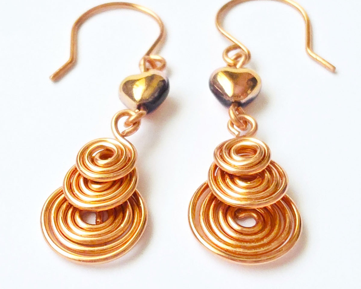 A pair of handmade copper dangle earrings with three coil pendants and gold hearts with french earrings hooks on white background  