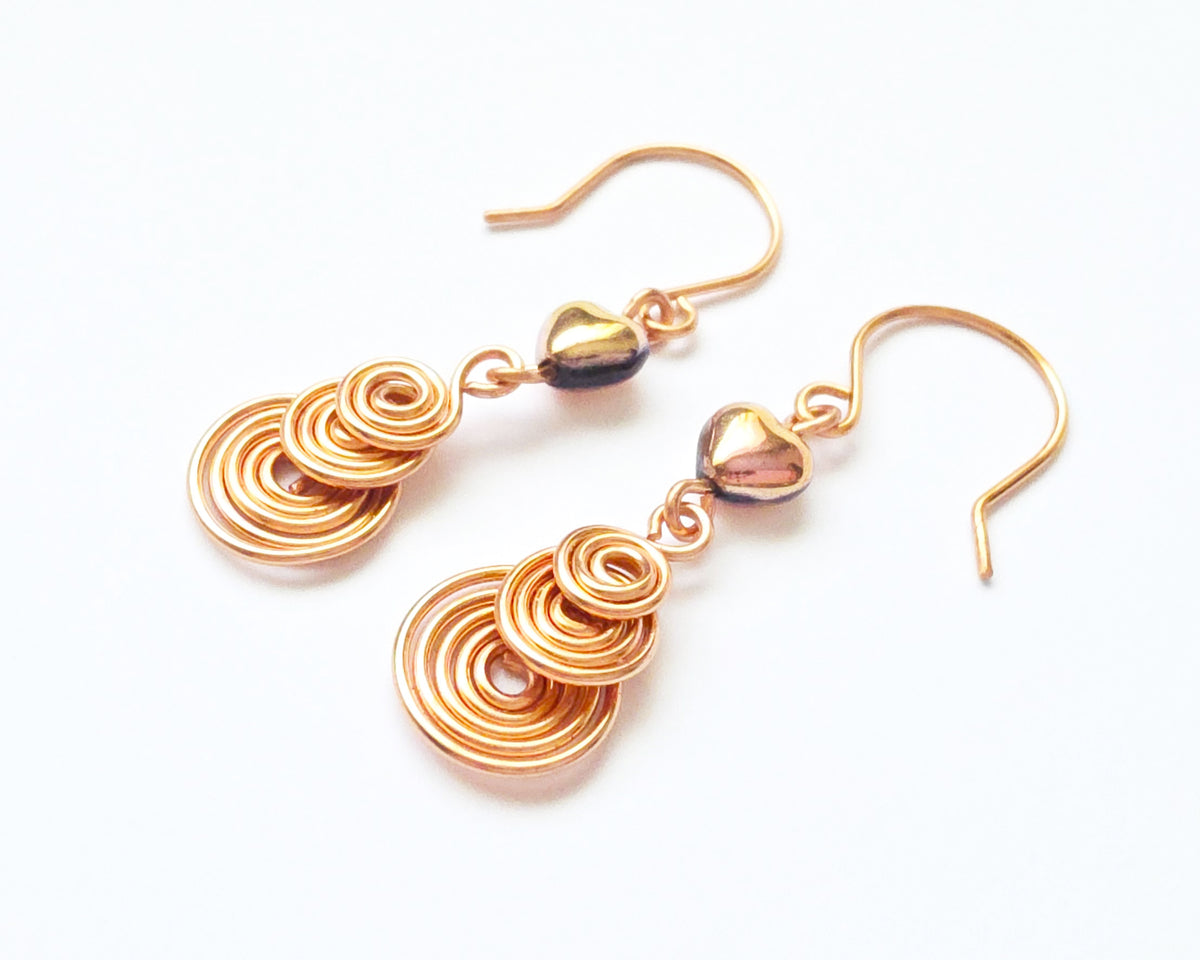 A pair of handmade copper dangle earrings with three coil pendants and gold hearts with french earrings hooks on white background  