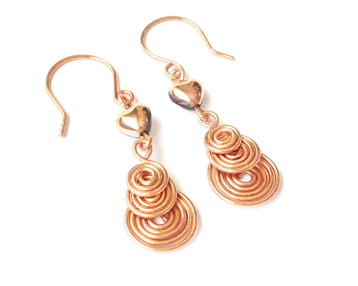 A pair of handmade copper dangle earrings with three coil pendants and gold hearts with french earrings hooks on white background  