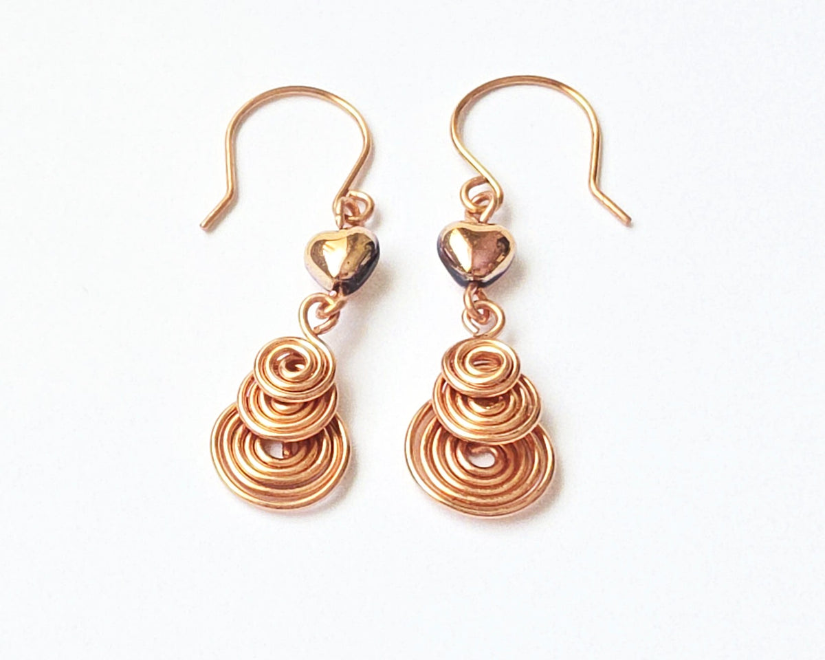 A pair of handmade copper dangle earrings with three coil pendants and gold hearts with french earrings hooks on white background  