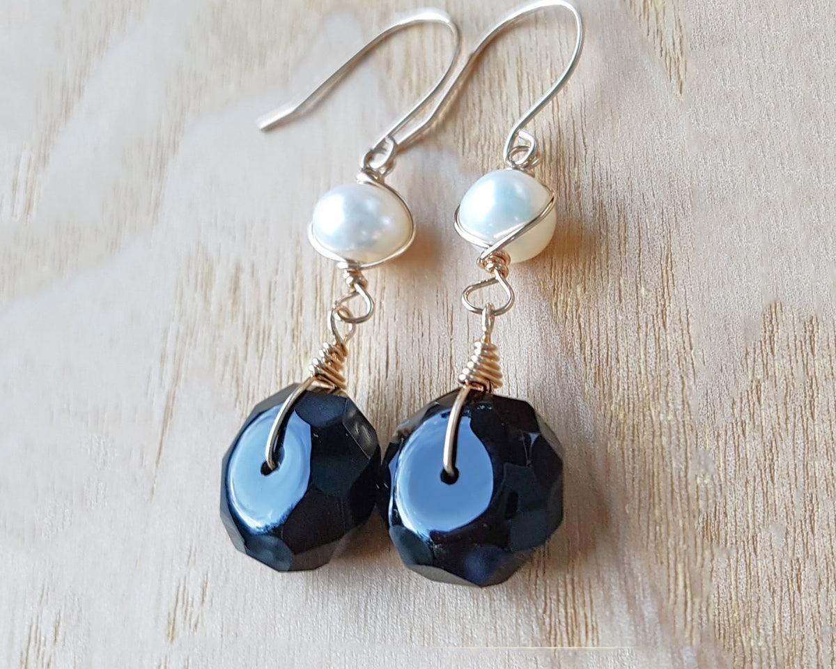 A pair of handmade Black Onyx and white Freshwater cultured Pearl earring wrapped with gold wire and french hooks on wood 