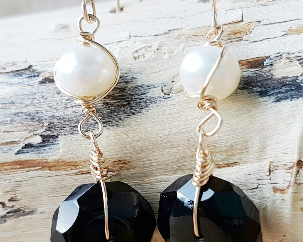 A pair of handmade Black Onyx and white Freshwater cultured Pearl earring wrapped with gold wire and french hooks on wood 