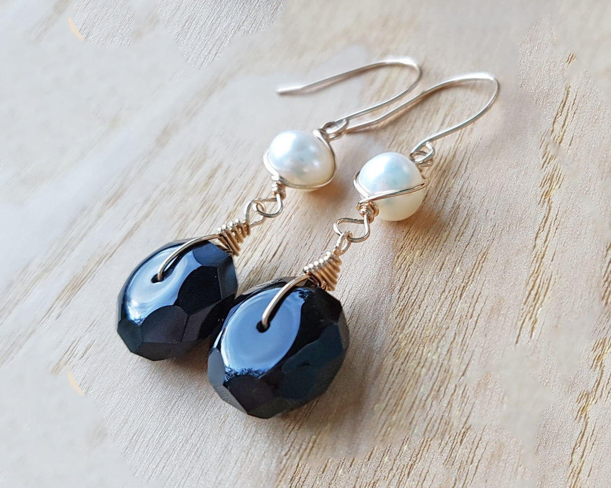 A pair of handmade Black Onyx and white Freshwater cultured Pearl earring wrapped with gold wire and french hooks on wood 