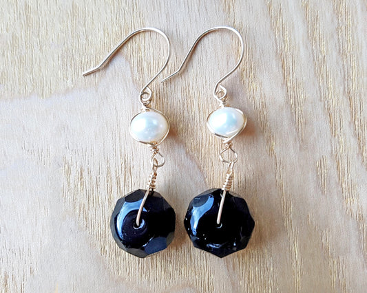 A pair of handmade Black Onyx and white Freshwater cultured Pearl earring wrapped with gold wire and french hooks on wood 