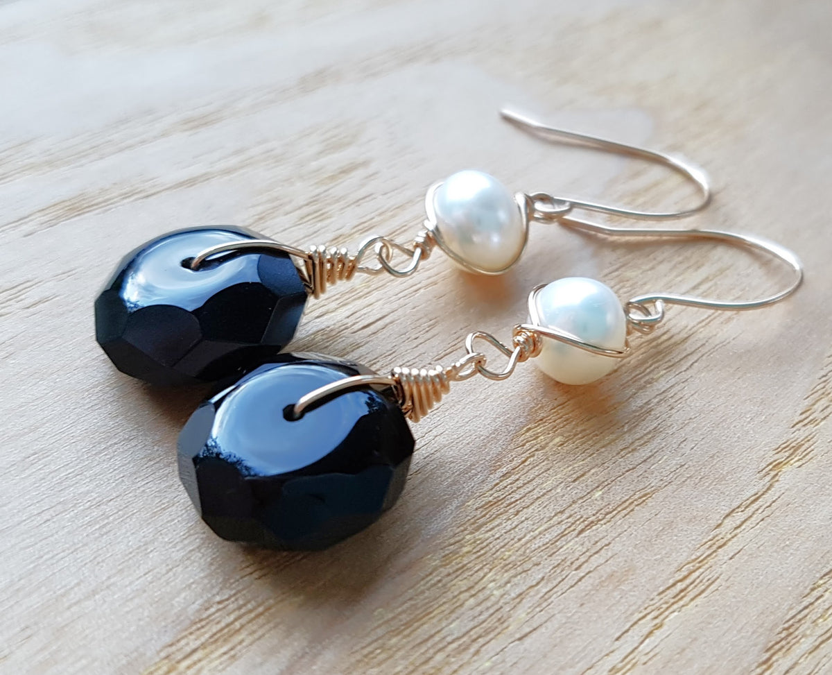 A pair of handmade Black Onyx and white Freshwater cultured Pearl earring wrapped with gold wire and french hooks on wood 