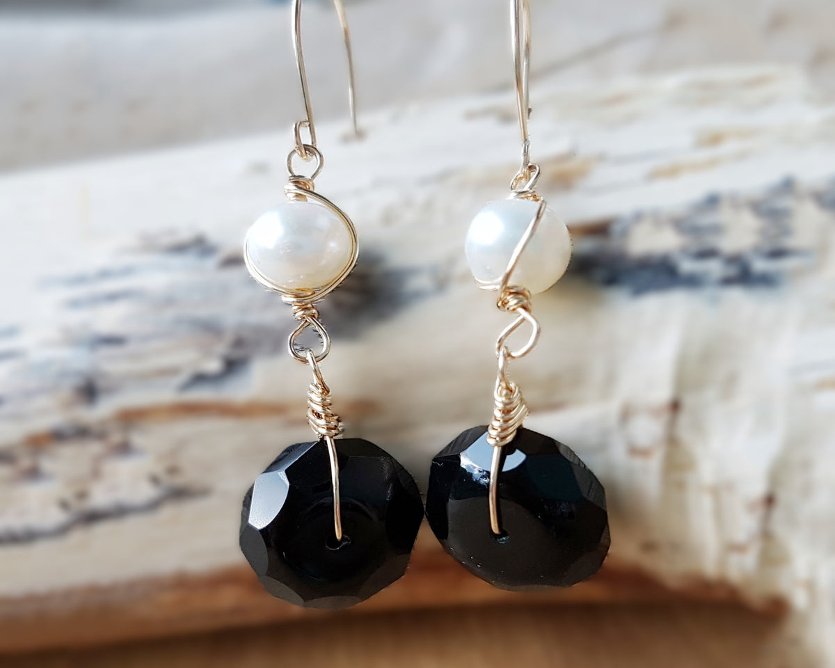 A pair of handmade Black Onyx and white Freshwater cultured Pearl earring wrapped with gold wire and french hooks on wood 