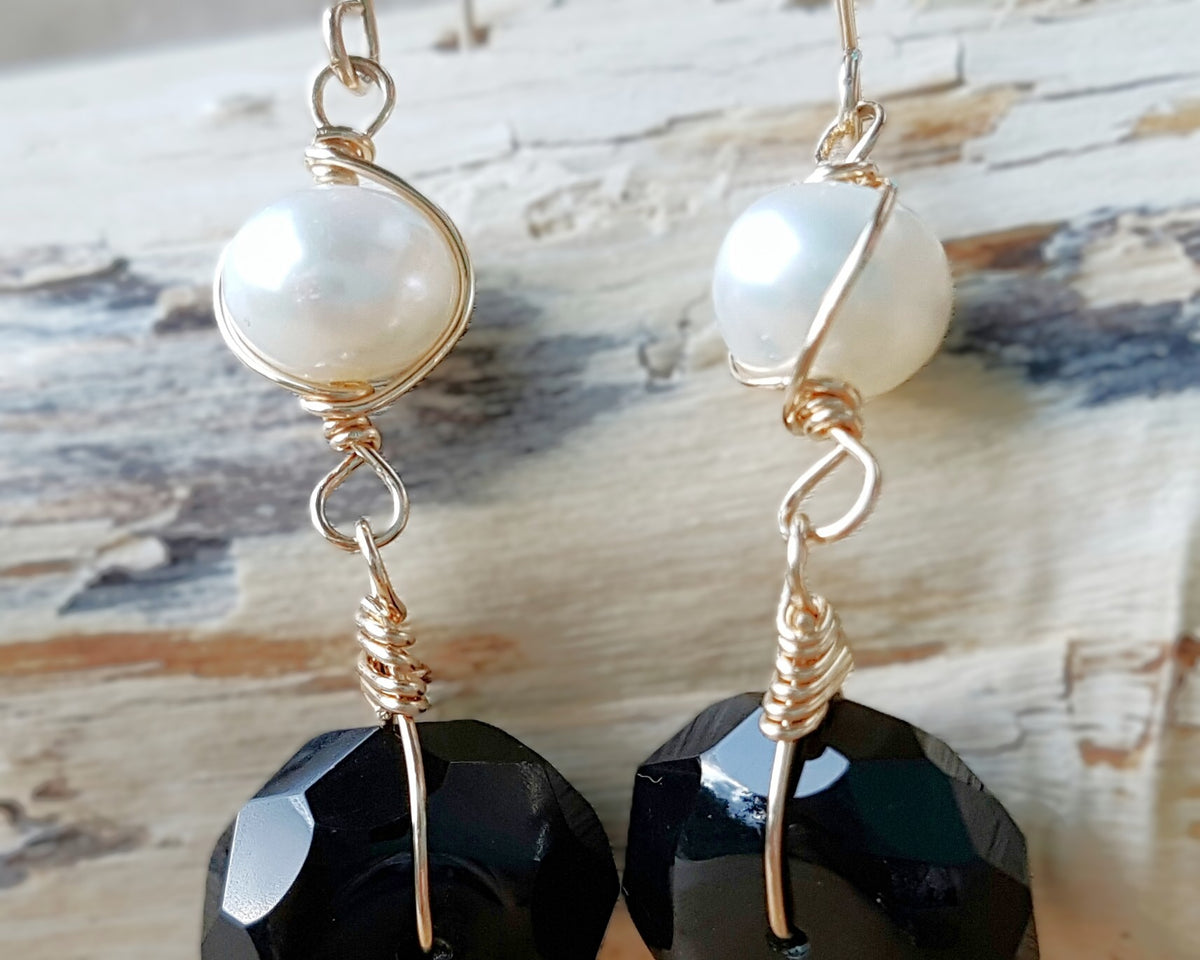 A pair of handmade Black Onyx and white Freshwater cultured Pearl earring wrapped with gold wire and french hooks on wood 