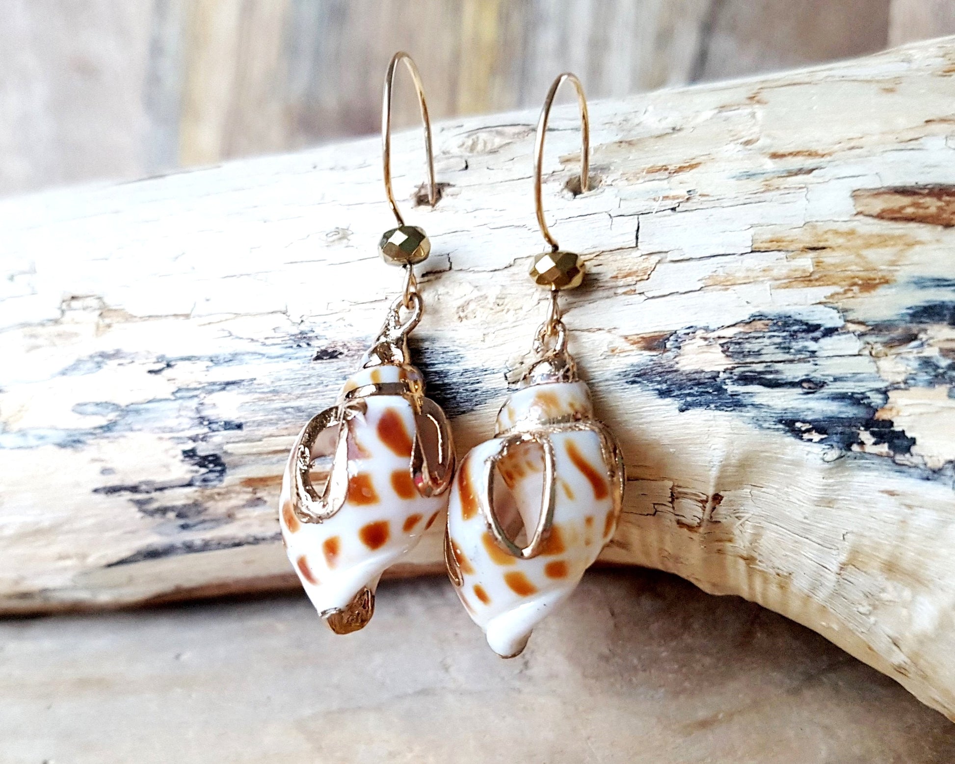 A pair of long Shell Dangle earring with shells cut and detailed with  gold and sparkly gold-plated hematite, french style earrings hooks, displayed on beach wood