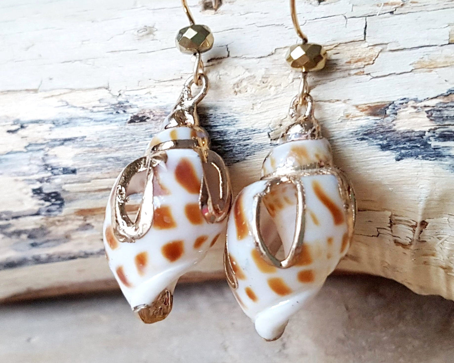 A pair of long Shell Dangle earring with shells cut and detailed with gold and sparkly gold-plated hematite, french style earrings hooks, displayed on beach wood