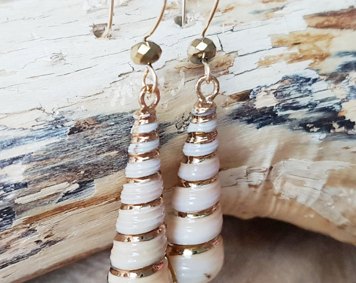 Golden Ocean Shell Dangle Earrings with gold trimmed cone shaped natural shells and sparkly gold french earrings hooks, displayed on beach wood