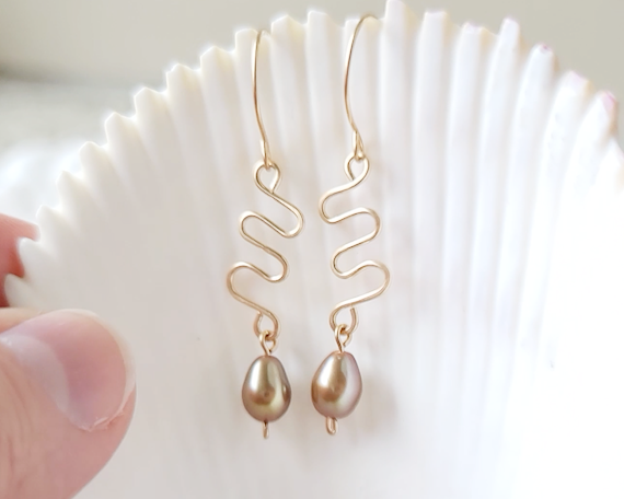 Long Gold Swirling, Wavy Design Earrings and drop shape gold Freshwater Cultured Pearls dangling from French style earring hooks, on white Shell