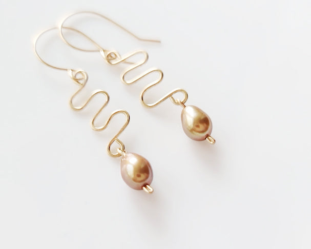 Long Gold Swirling, Wavy Design Earrings and drop shape gold Freshwater Cultured Pearls dangling from French style earring hooks, on white Background  