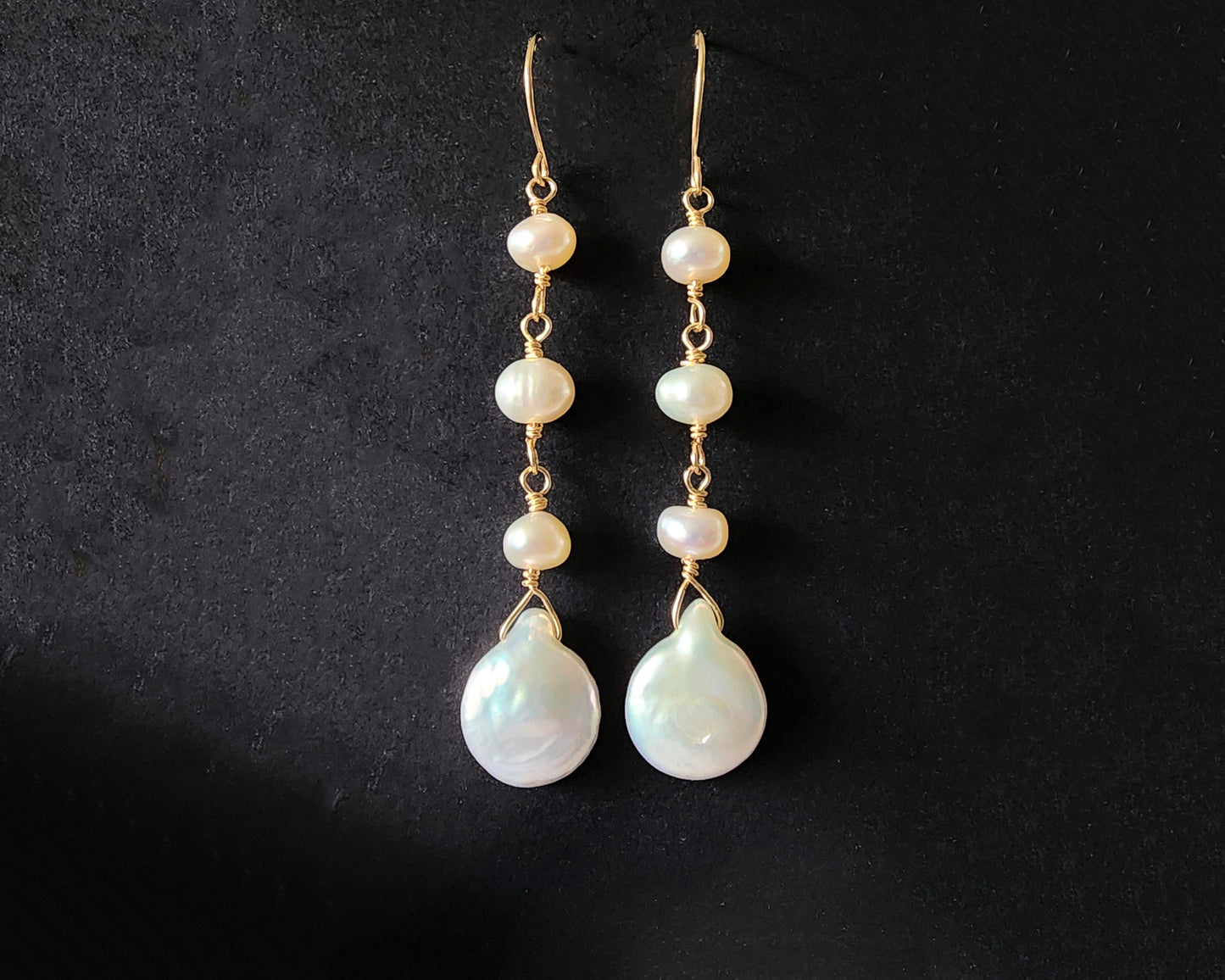 A pair of long handmade Art Deco style white pearl  gold dangle earrings,  French earrings hooks on black background 