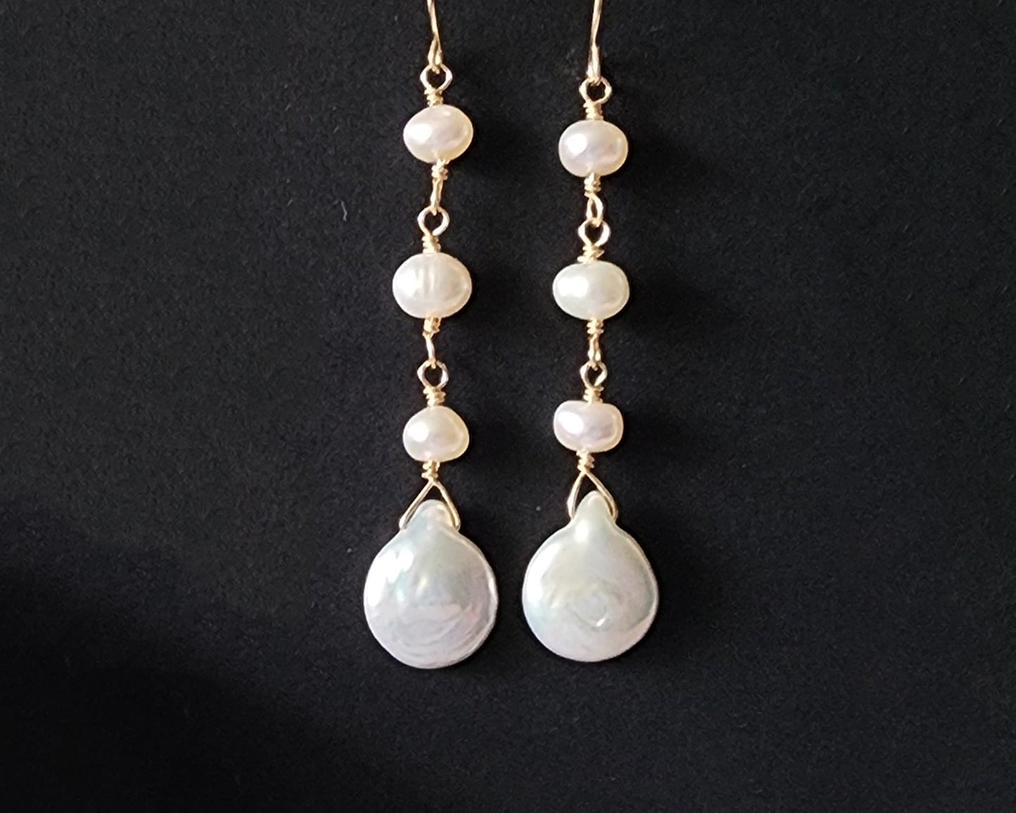 A pair of long handmade Art Deco style white pearl  gold dangle earrings,  French earrings hooks on black background 