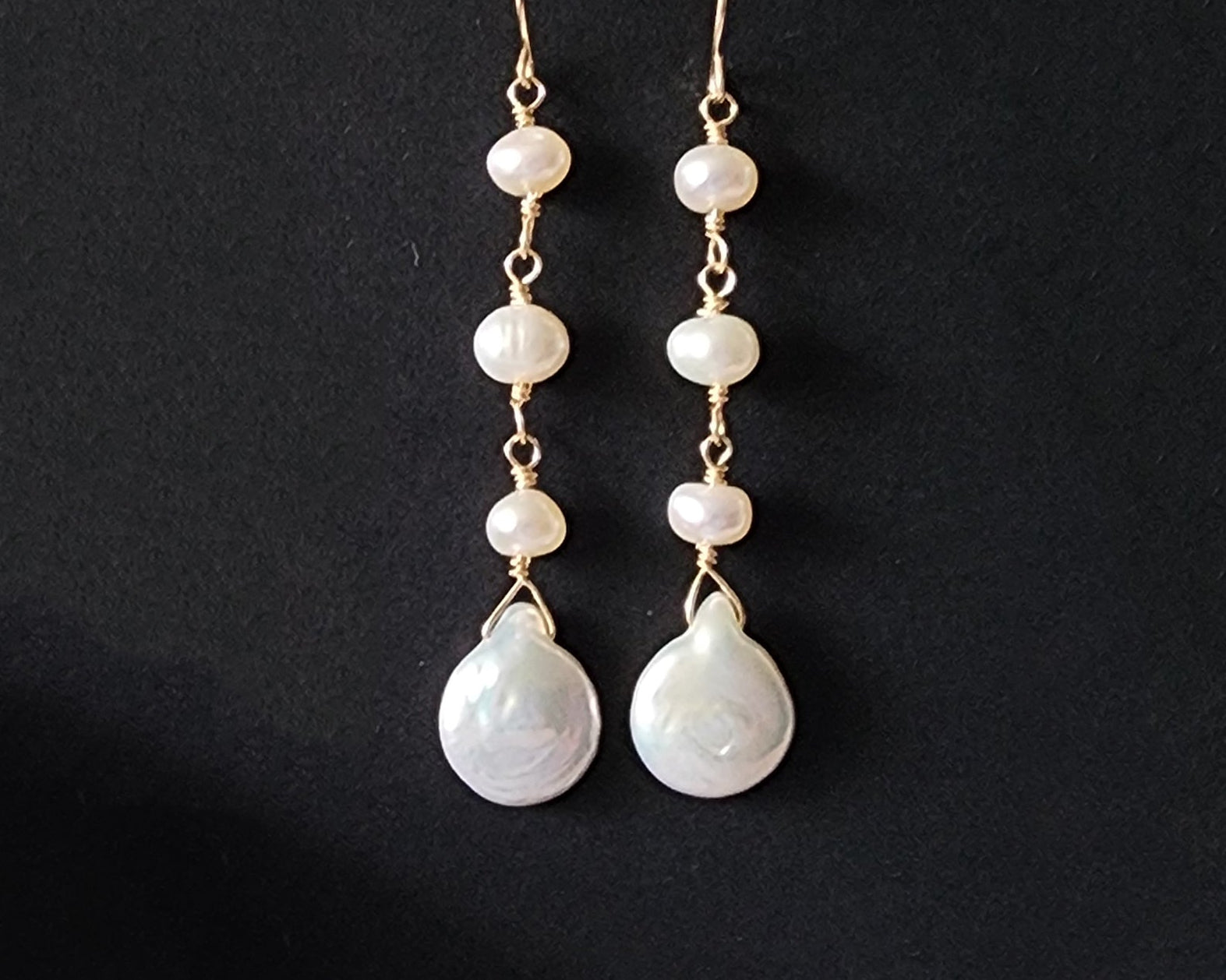 A pair of long handmade Art Deco style white pearl  gold dangle earrings,  French earrings hooks on black background 
