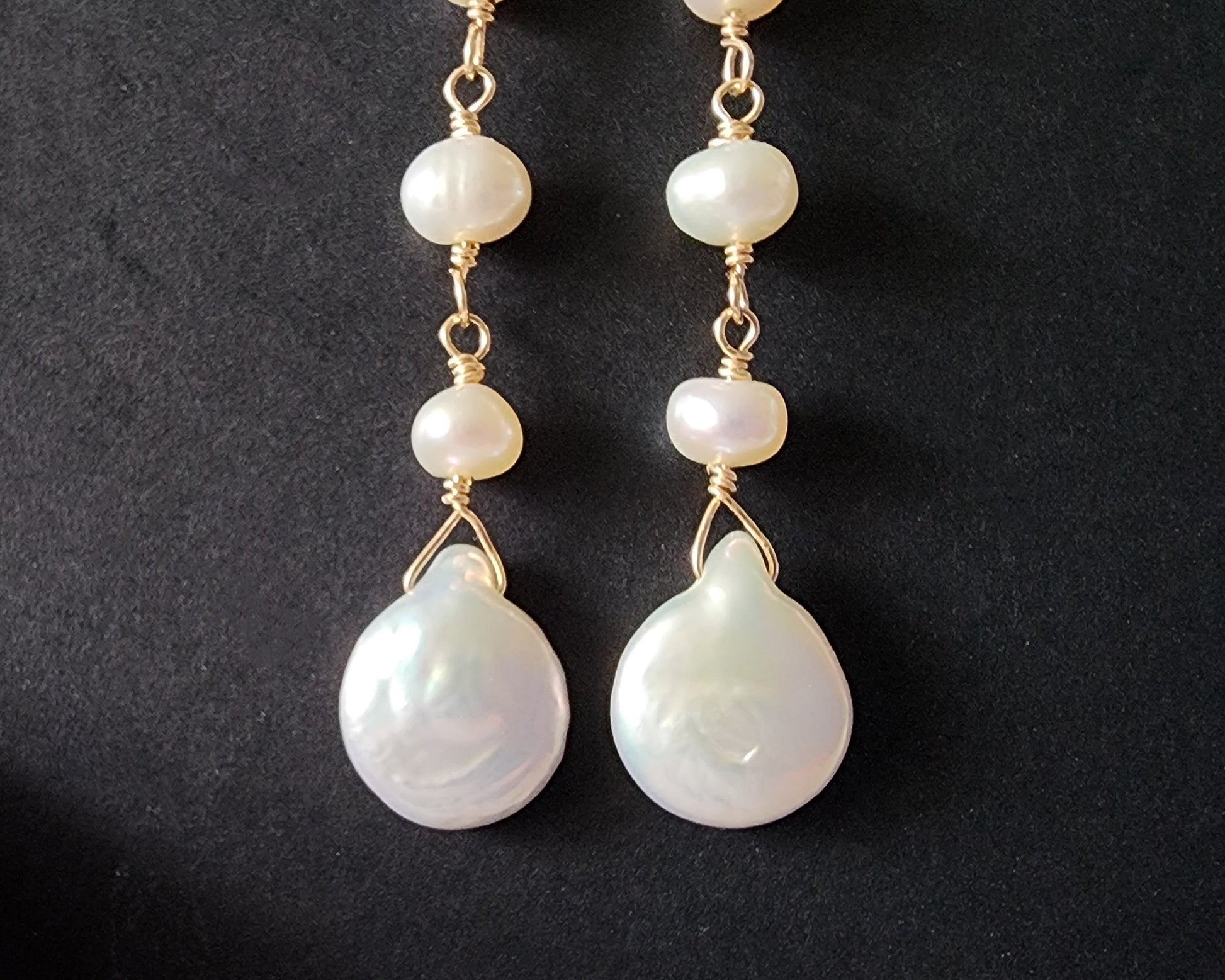 A pair of long handmade Art Deco style white pearl  gold dangle earrings,  French earrings hooks on black background 