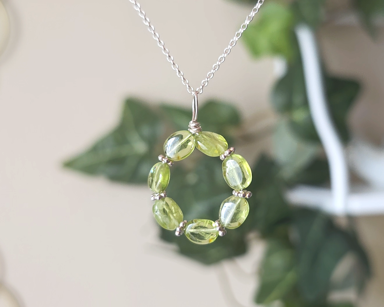 Round Peridot beaded pendant with oval shaped translucent Peridot stones and fancy sterling silver beads in between on a sterling silver rolo chain with plants in the background