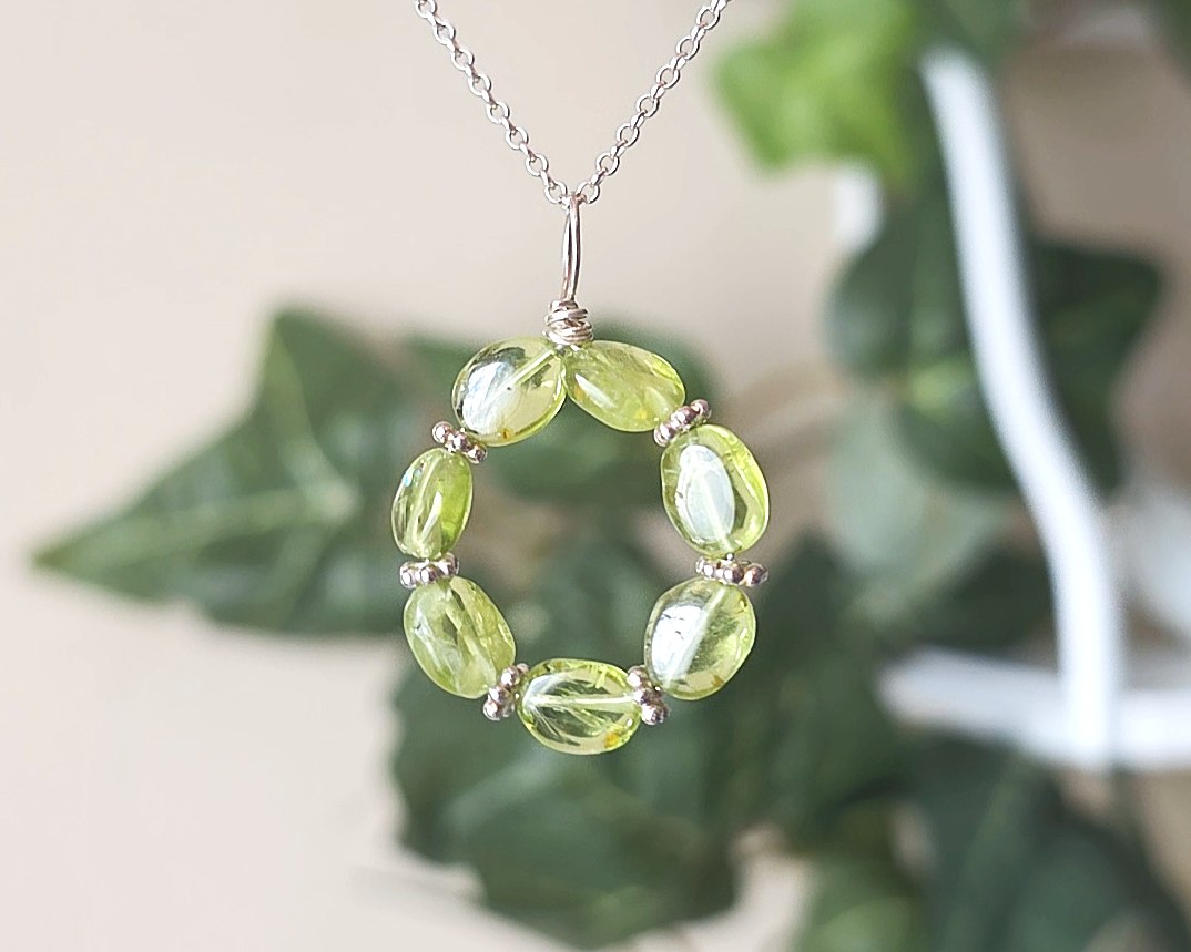 Round Peridot beaded pendant with oval shaped translucent Peridot stones and fancy sterling silver beads in between on a sterling silver rolo chain with plants in the background