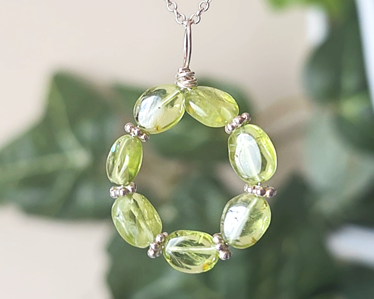 Round Peridot beaded pendant with oval shaped translucent Peridot stones and fancy sterling silver beads in between on a sterling silver rolo chain with plants in the background