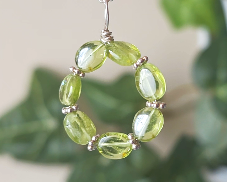 Round Peridot beaded pendant with oval shaped translucent Peridot stones and fancy sterling silver beads in between on a sterling silver rolo chain with plants in the background