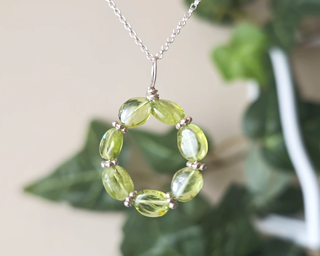 Round Peridot beaded pendant with oval shaped translucent Peridot stones and fancy sterling silver beads in between on a sterling silver rolo chain with plants in the background