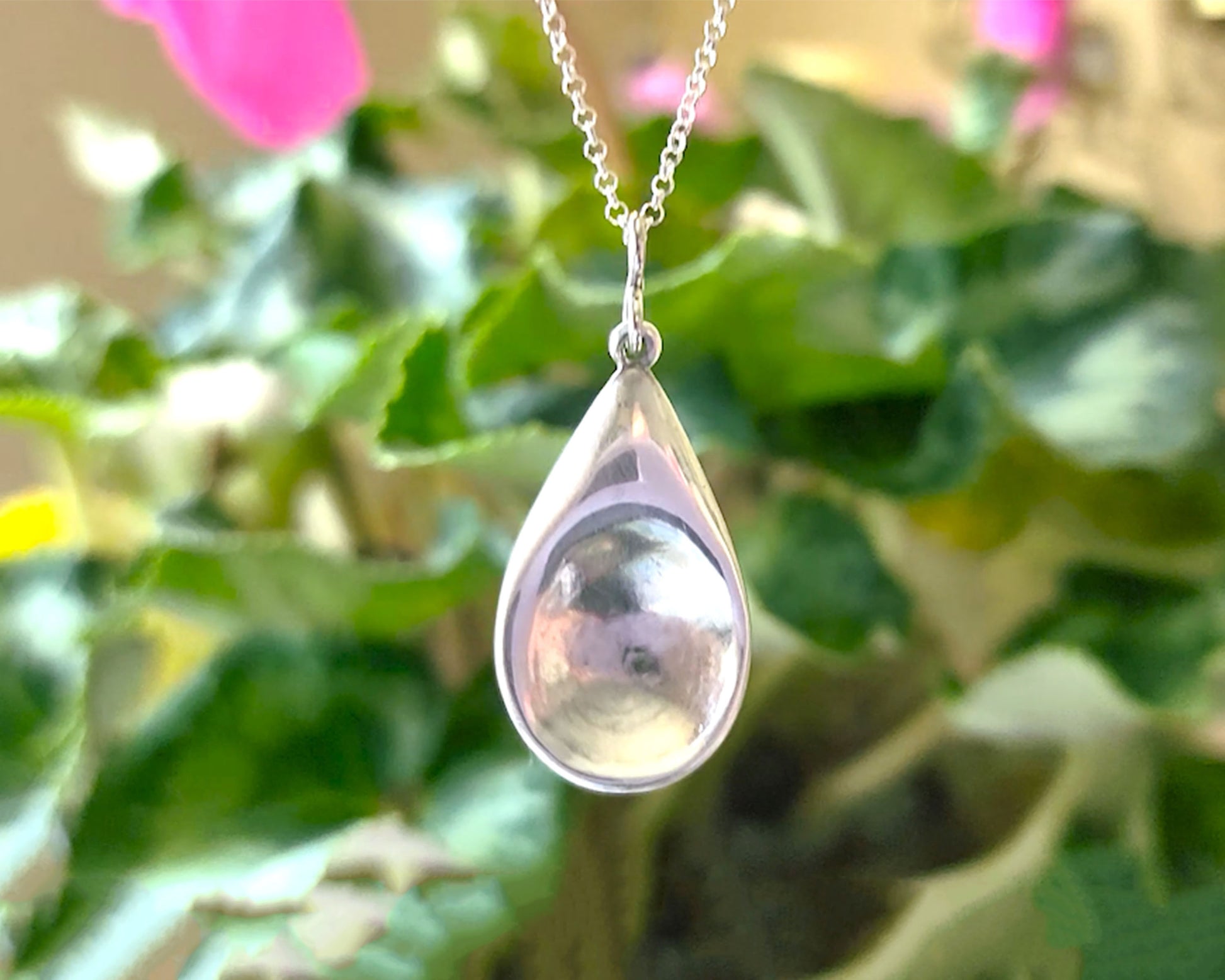 Love inspired spoon shaped Sterling Silver pendant on rolo style chain with plant in background