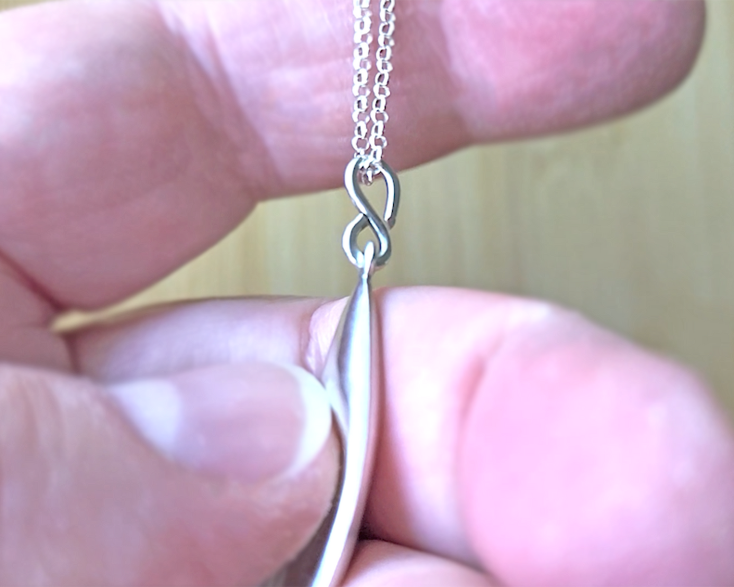 Love inspired spoon shaped Sterling Silver pendant on rolo style chain on hand 