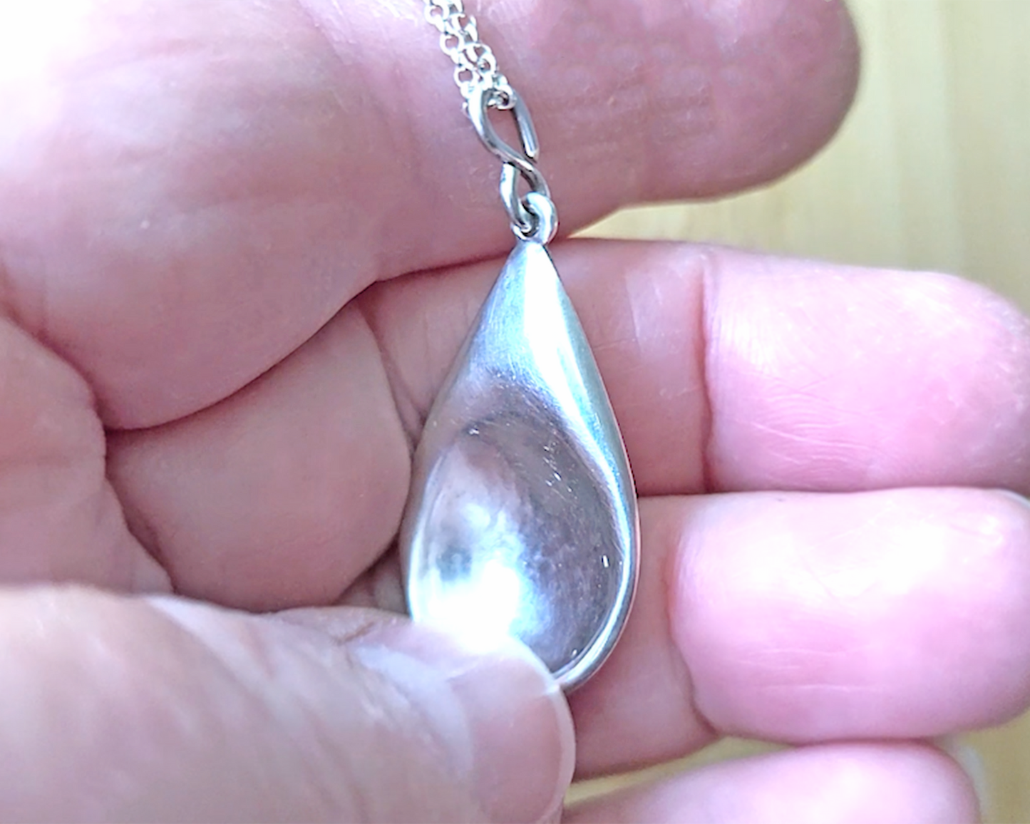 Love inspired spoon shaped Sterling Silver pendant on rolo style chain on hand 