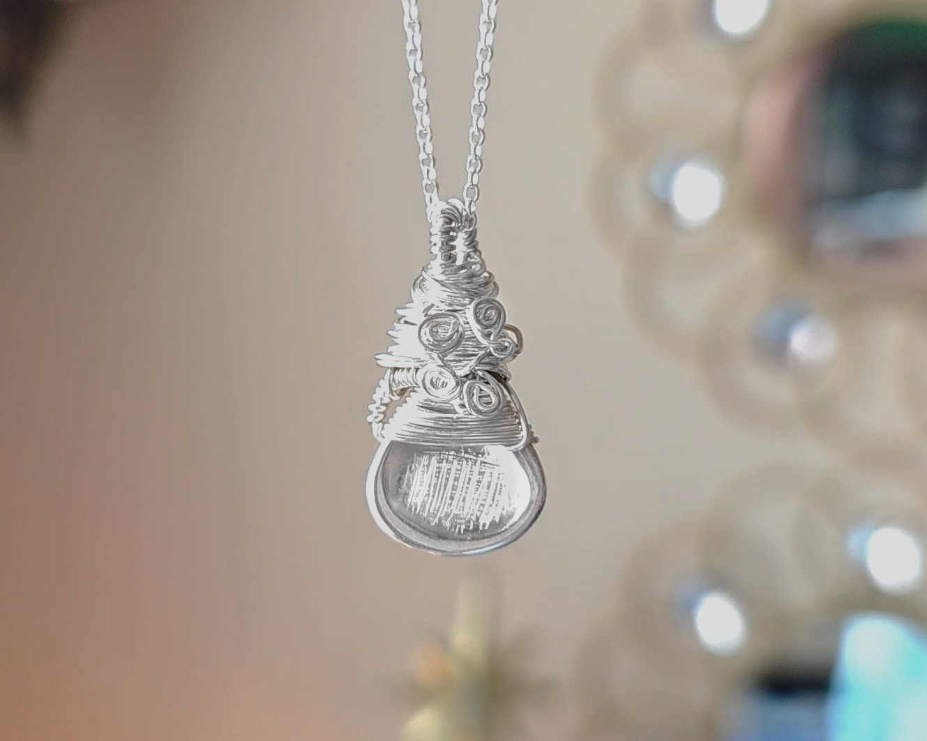 Sterling Silver Sculptural and Wire Wrapped Pendant with coils and texture on a rolo style chain with beige blurred background 