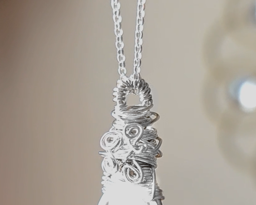 Sterling Silver Sculptural and Wire Wrapped Pendant with coils and texture on a rolo style chain with beige blurred background 