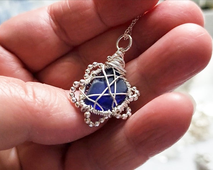 Sapphire Blue Beach Glass Flower Pendant- Freshwater Sea Glass
, Sterling Sivler Wire and tiny faceted Sterling silver beads to create a flower like design. Pendant dangles on Sterling Silver rolo chain. 
