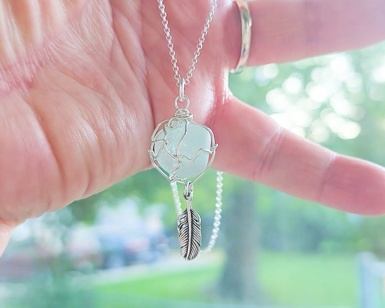 Silver Pendant with Aqua Blue Sea Glass and dangling Silver Feather on Silver Rolo chain displayed in hand