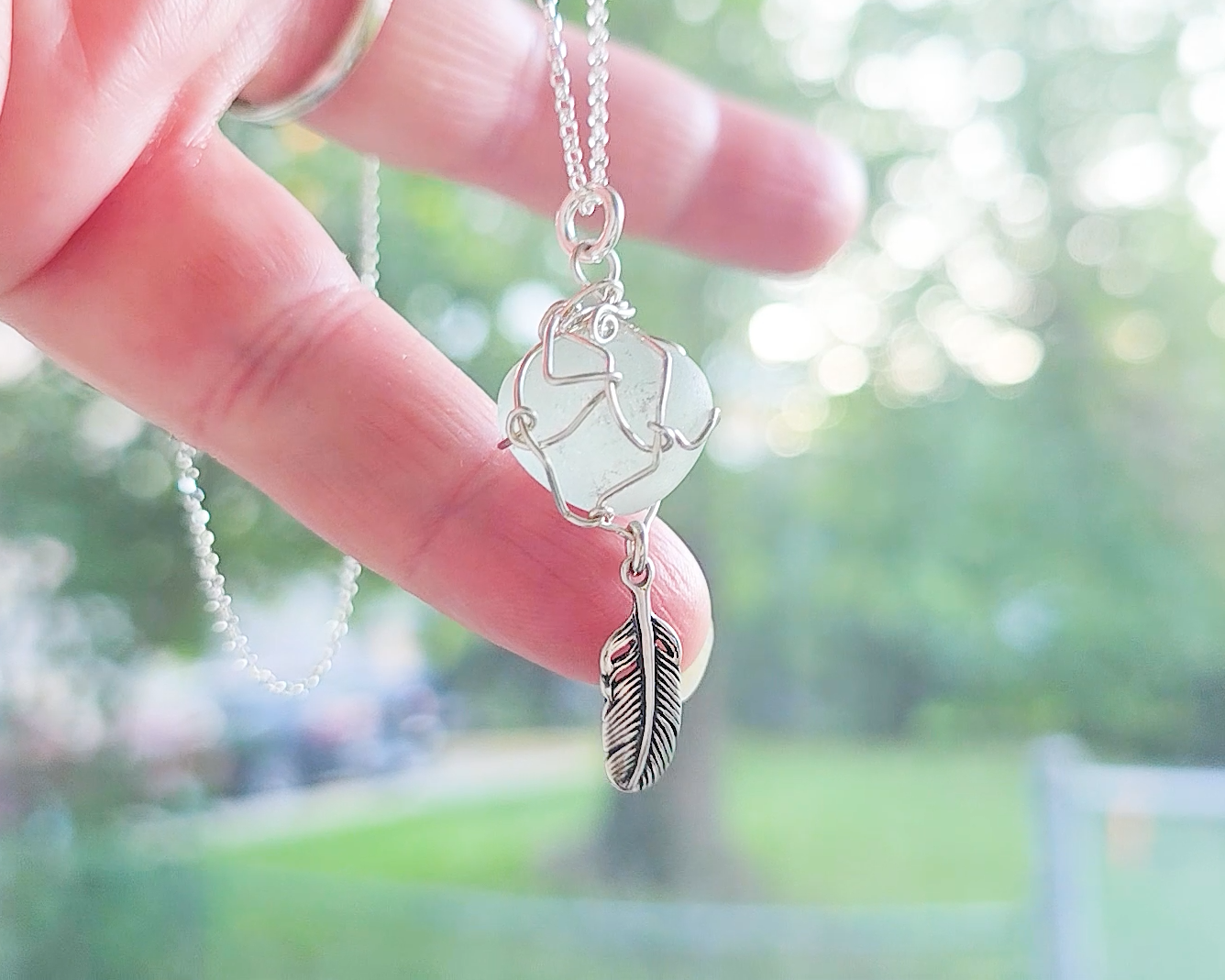 Silver Pendant with Aqua Blue Sea Glass and dangling Silver Feather on Silver Rolo chain displayed in hand