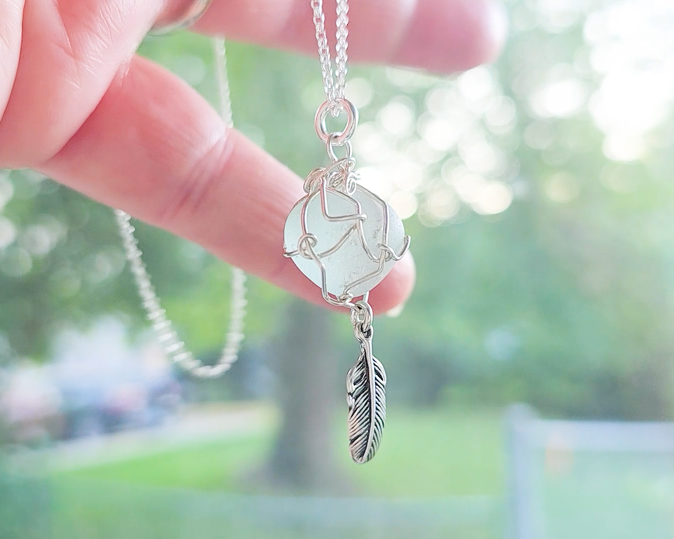 Silver Pendant with Aqua Blue Sea Glass and dangling Silver Feather on Silver Rolo chain displayed in hand