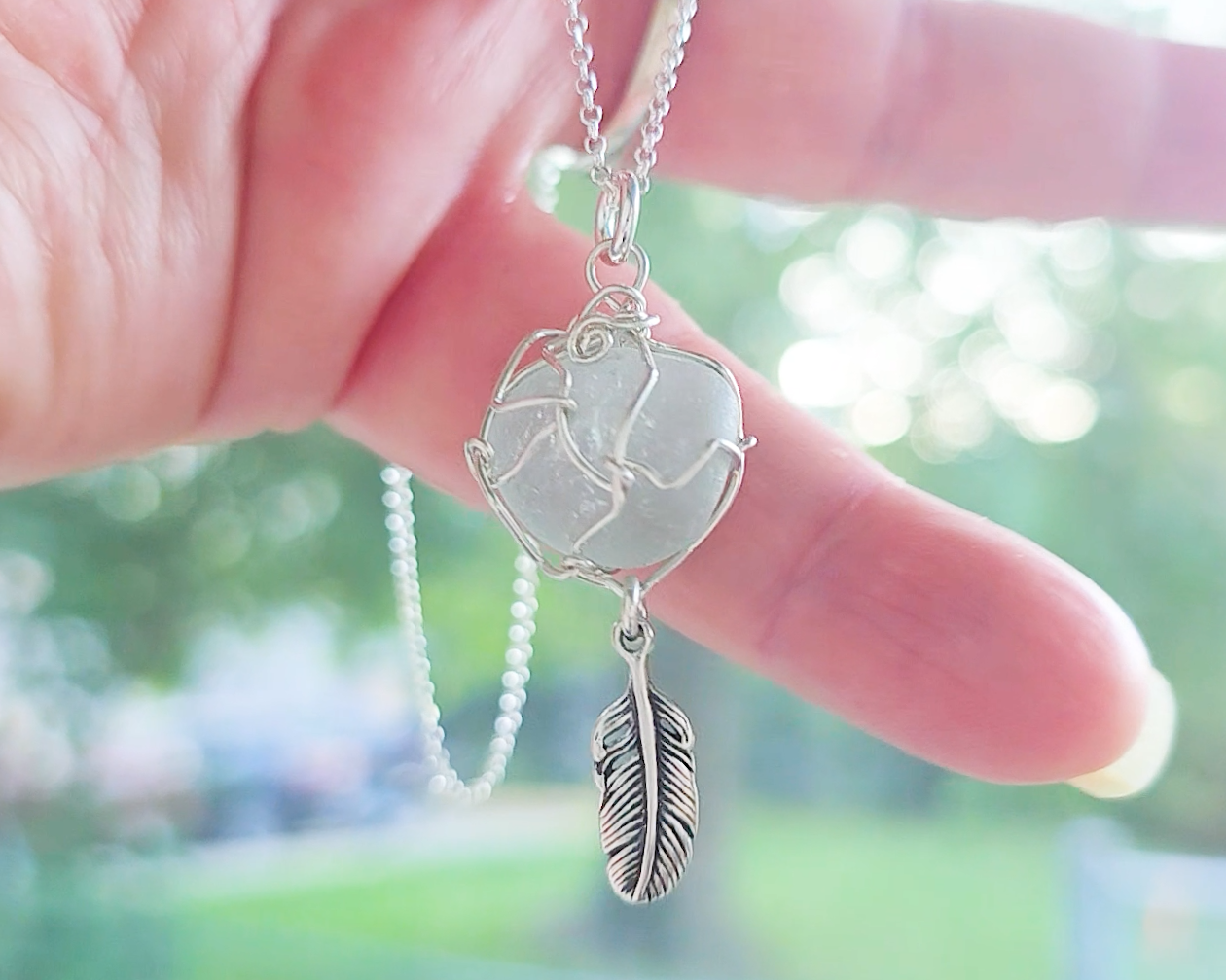 Silver Pendant with Aqua Blue Sea Glass and dangling Silver Feather on Silver Rolo chain displayed in hand