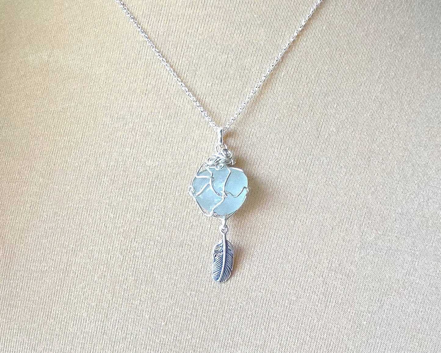 Silver Pendant with Aqua Blue Sea Glass and dangling Silver Feather on Silver Rolo chain displayed on beige