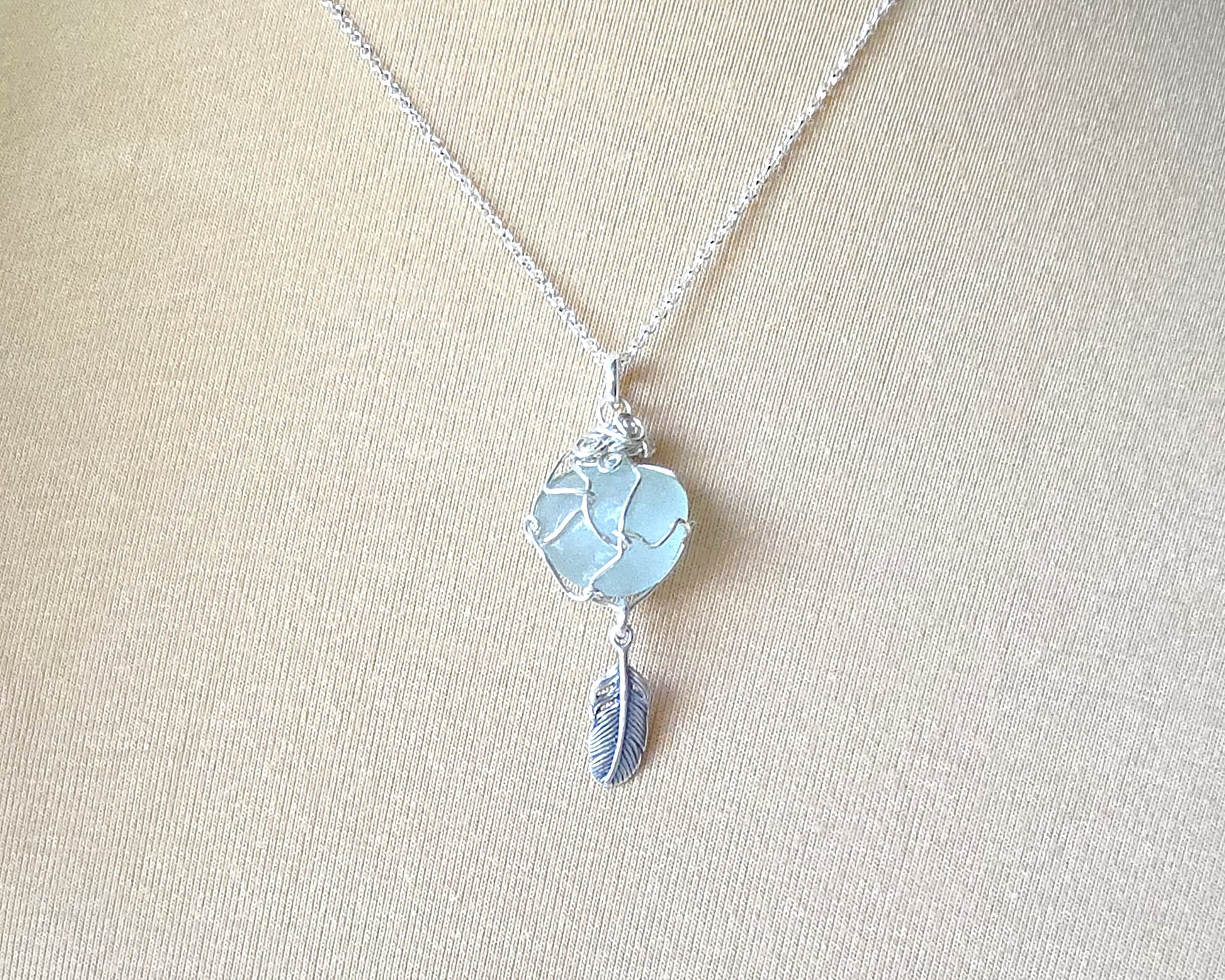 Silver Pendant with Aqua Blue Sea Glass and dangling Silver Feather on Silver Rolo chain displayed on beige