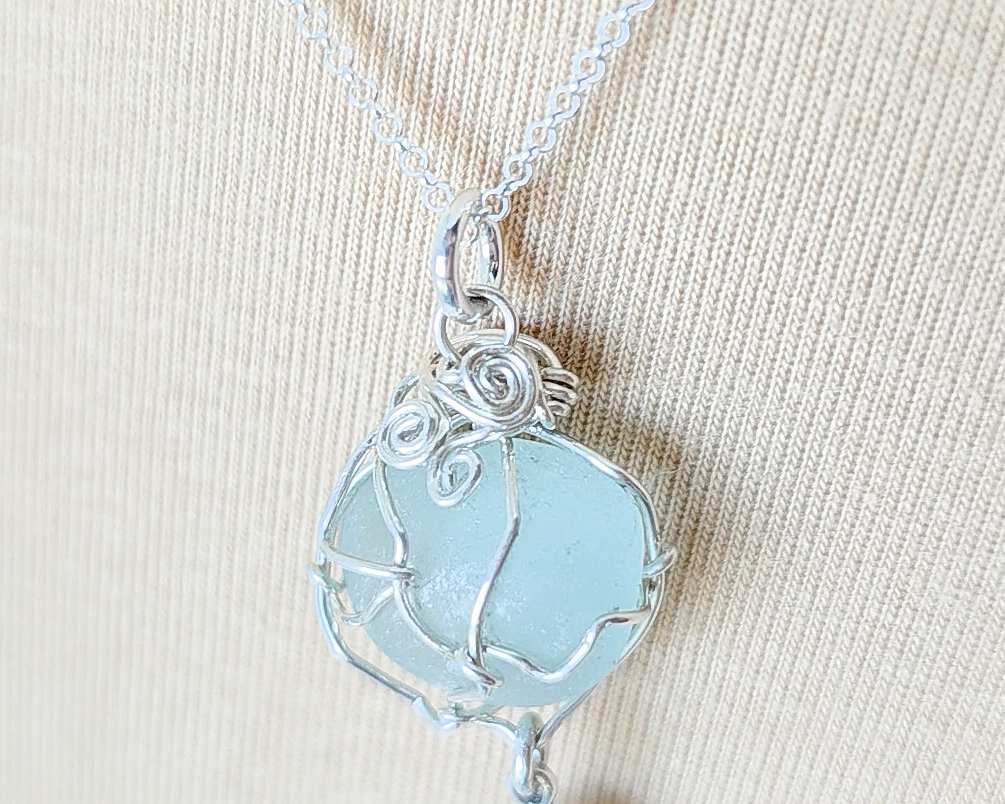 Silver Pendant with Aqua Blue Sea Glass and dangling Silver Feather on Silver Rolo chain displayed on beige