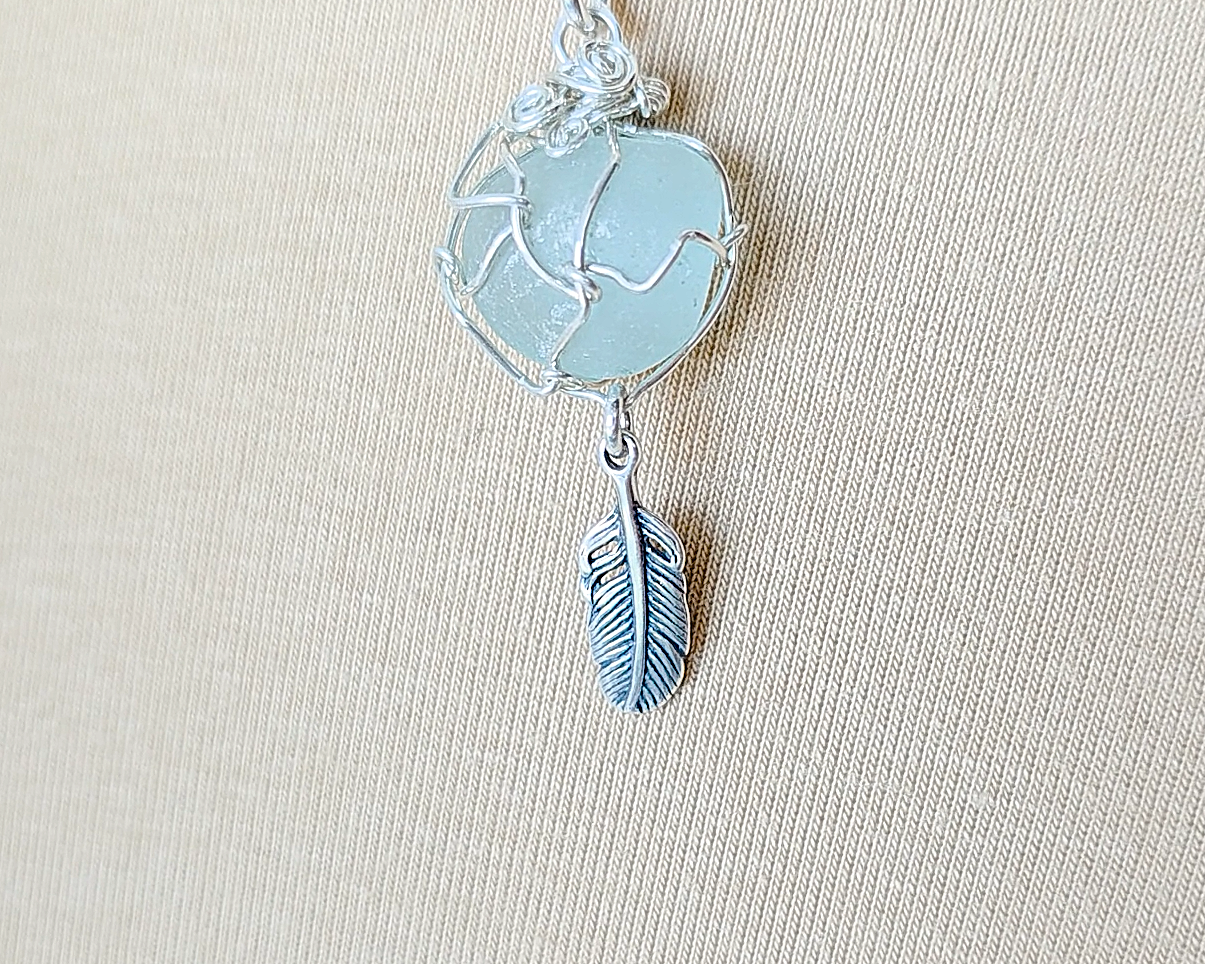 Silver Pendant with Aqua Blue Sea Glass and dangling Silver Feather on Silver Rolo chain displayed on beige